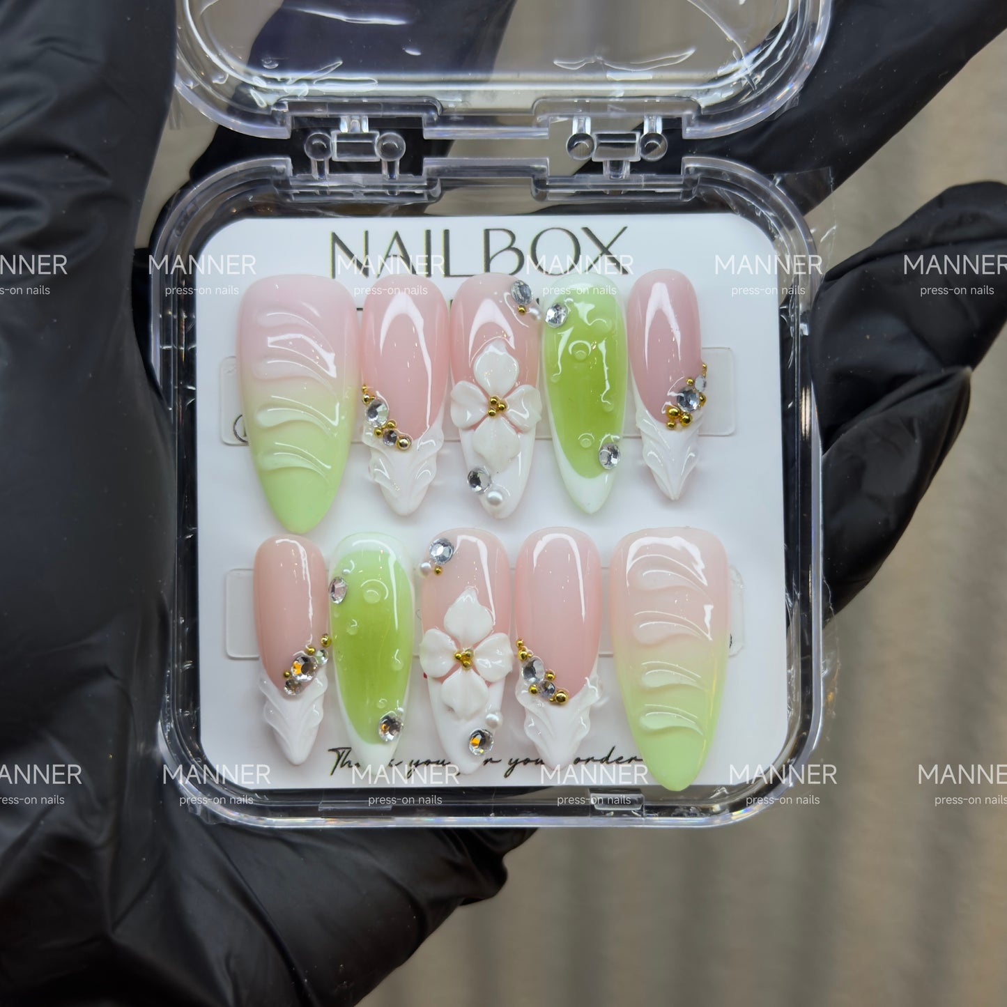 Handmade glossy almond press-on nails with blush pink and lime green gradient, embossed texture, sculpted white flowers, crystals and gold accents.